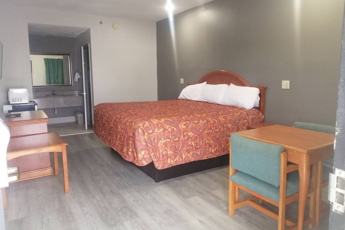 A hotel room with a bed, a desk, a chair, a small table, and a mirror.