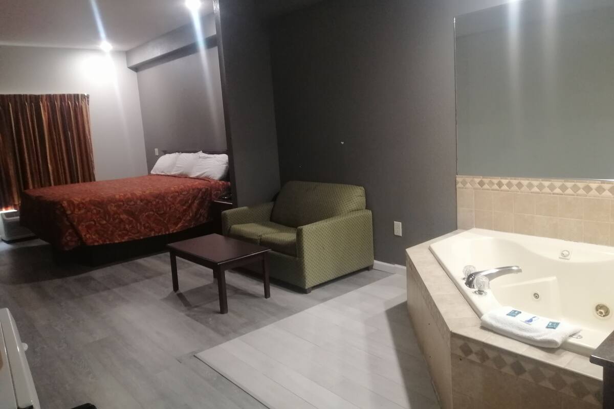 A hotel room with a bed, a green armchair, a small table, and a bathtub.