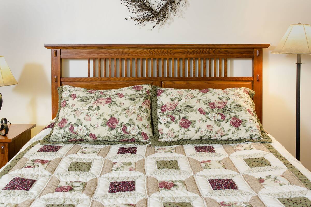 A bed with a floral quilt and wooden headboard, a bedside lamp, and a wall-mounted decoration.