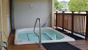 Ein Whirlpool auf einer Holzterrasse mit Holzumzäunung und einem Schild mit der Aufschrift 'KEIN BADEMEISTER ANWEISEND'.