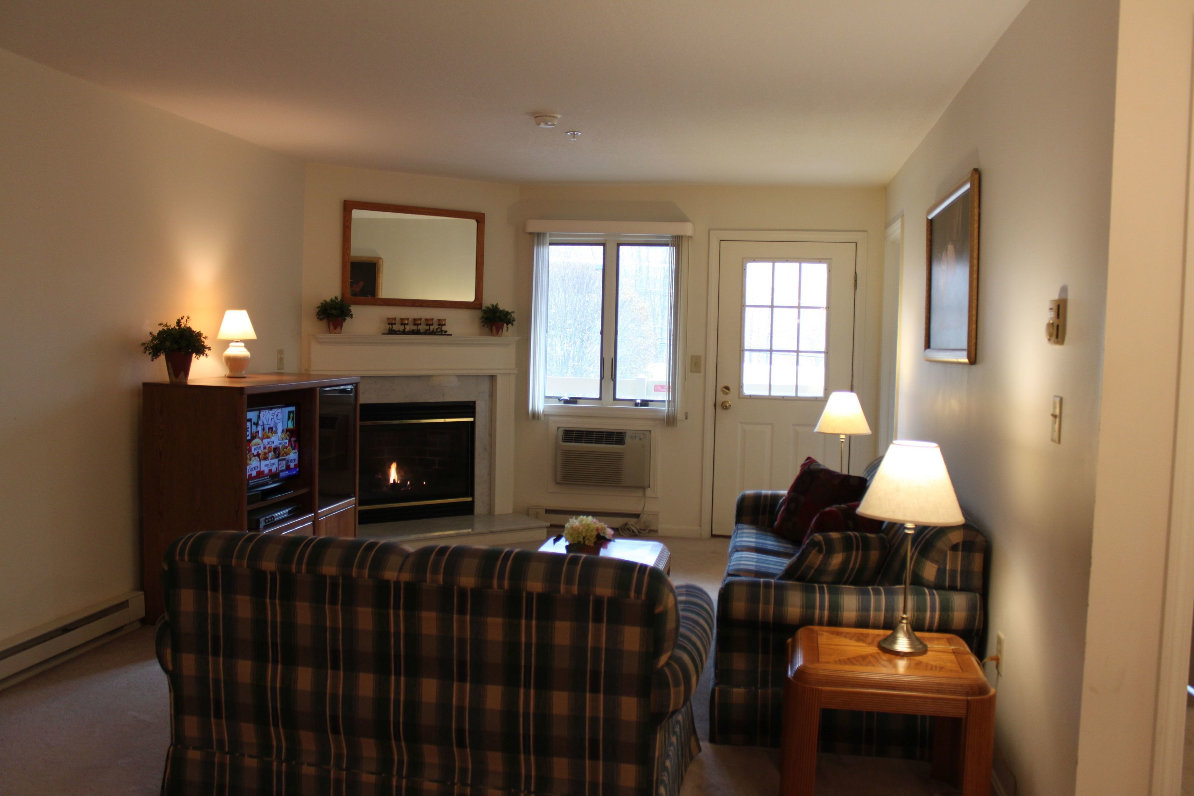 A living room with a fireplace, plaid furniture, and a television.