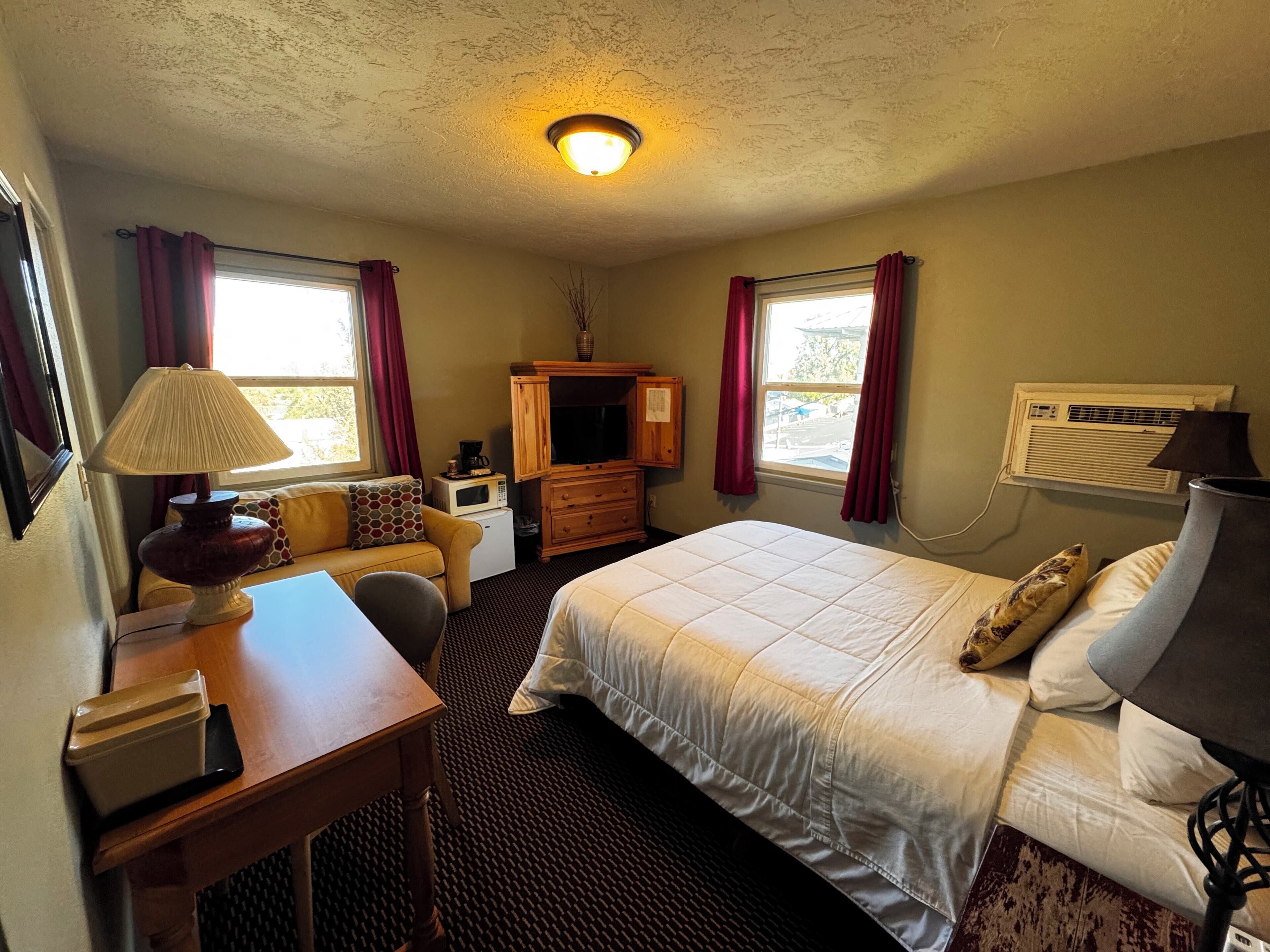 A hotel room with a bed, a desk, a chair, a television, a dresser, and a window with curtains.