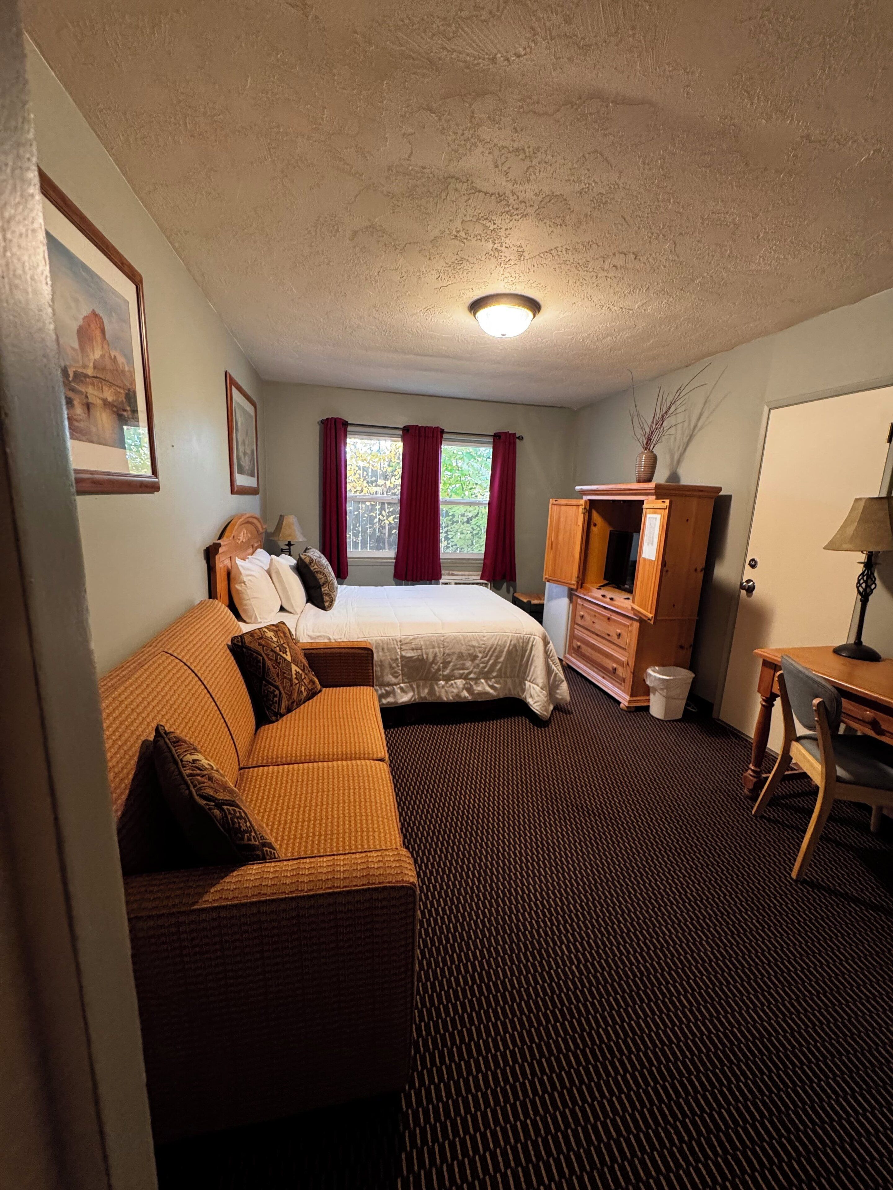 A hotel room with a bed, a sofa, a desk, and a dresser.