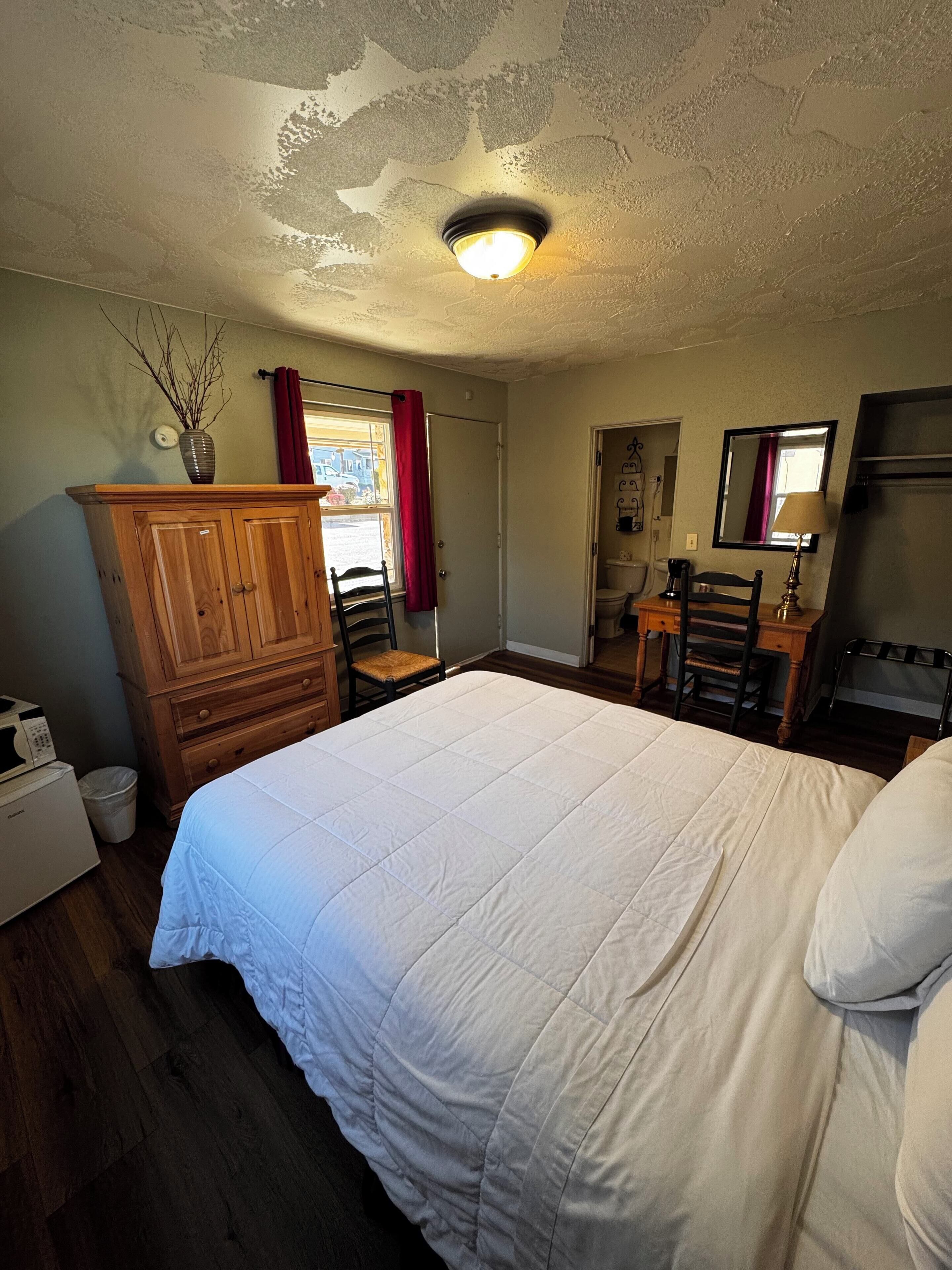 Un dormitorio con una cama grande, cómoda de madera y un escritorio con sillas.