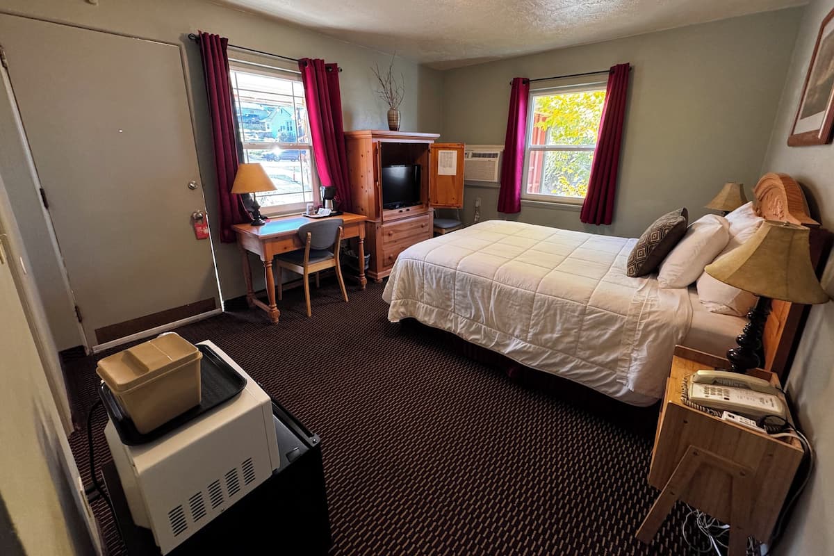 A hotel room with a bed, desk, chair, TV, and a small kitchenette area.