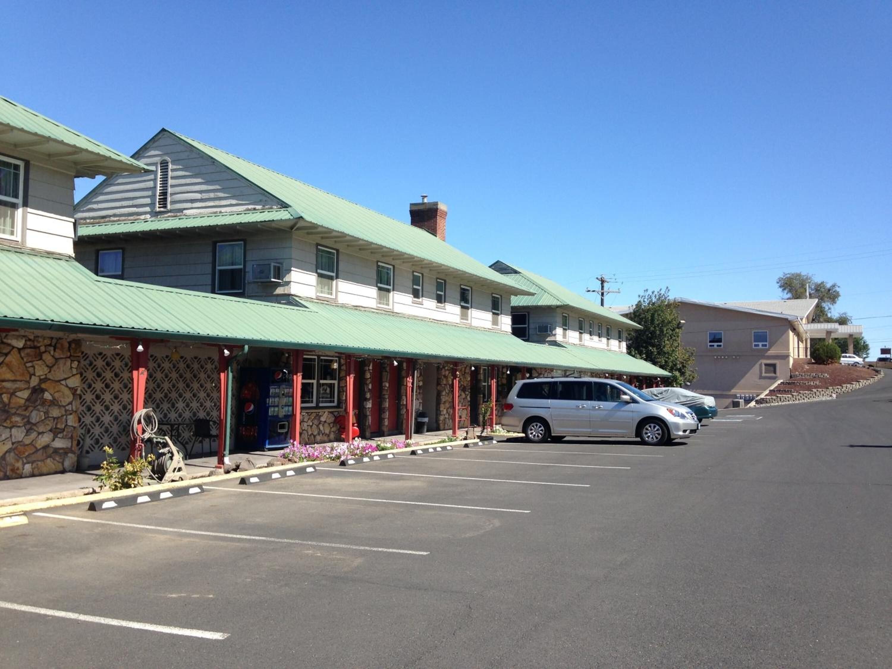 A two-story building with a green roof and a stone facade. There is a parking lot in front with several cars parked.
