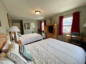A hotel room with two beds, a desk, a chair, a television, and a window with red curtains.