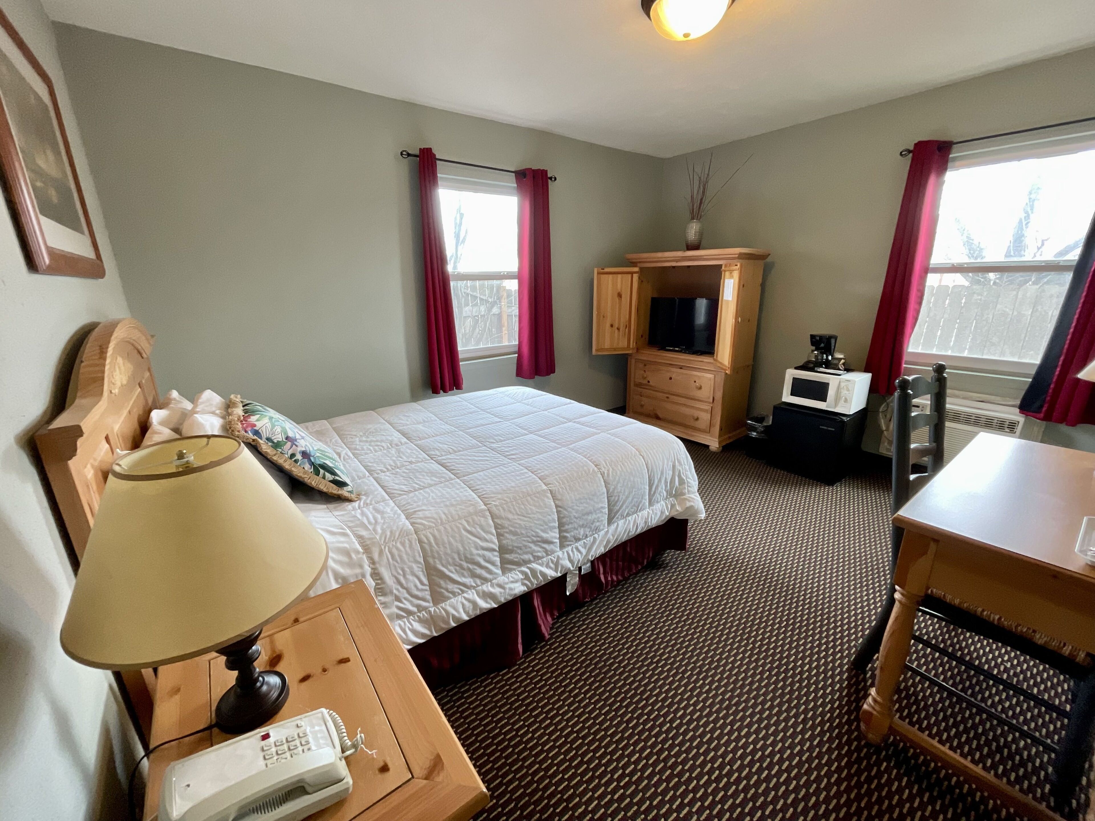 A hotel room with a bed, a desk with a lamp, a telephone, a television, and a microwave.