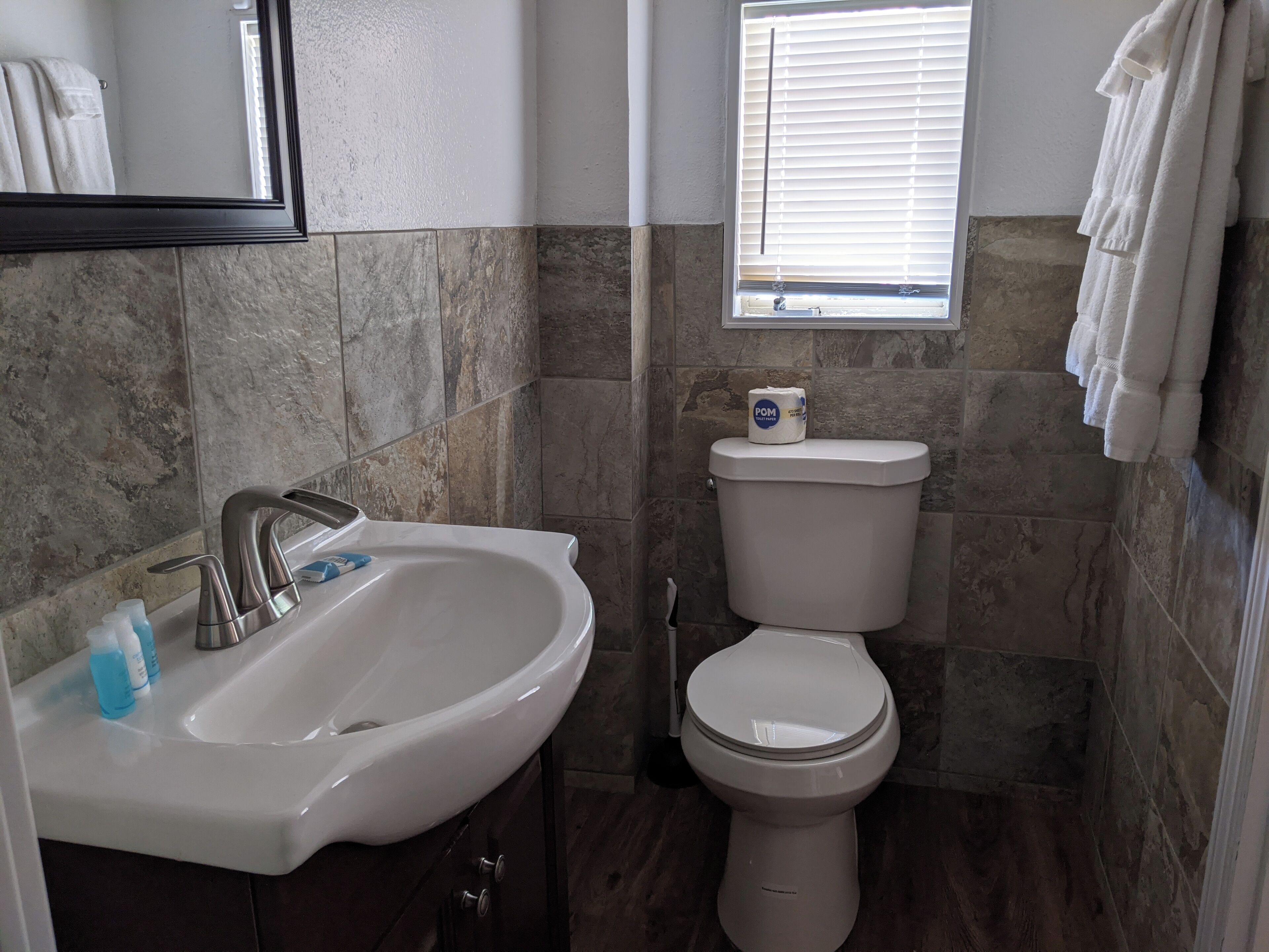 Une salle de bain avec un lavabo blanc, des toilettes et une fenêtre avec des stores.