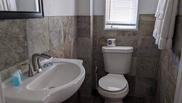 Une salle de bain avec un lavabo blanc, des toilettes et une fenêtre avec des stores.