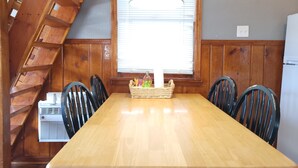 A dining area with a wooden table, black chairs, a wooden ladder, a window with blinds, a hanging light fixture, and a clock on the wall. - Stone Mountain Lodge and Cabins (Lyons)