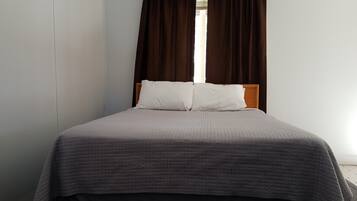 A single bed with a grey quilt, two white pillows, and dark brown curtains.