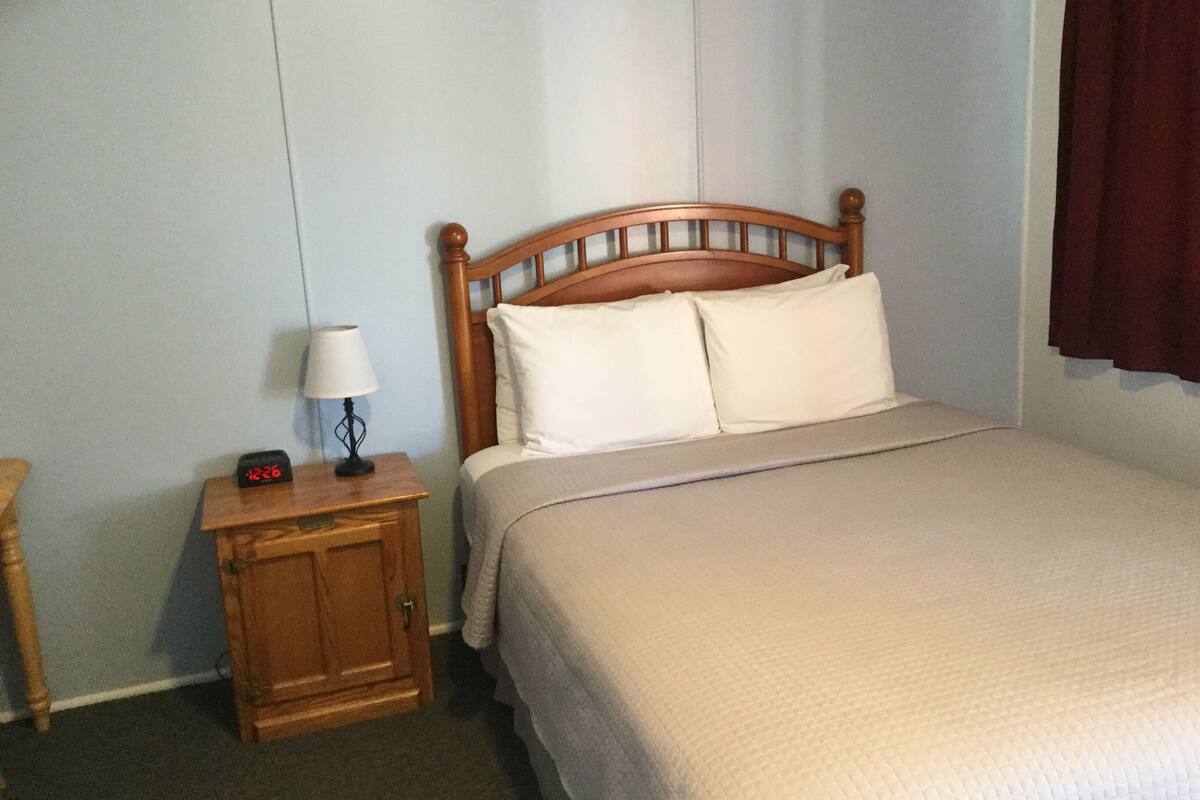 A bedroom with a wooden headboard, a bedside table with a lamp, and a bed with a beige blanket.