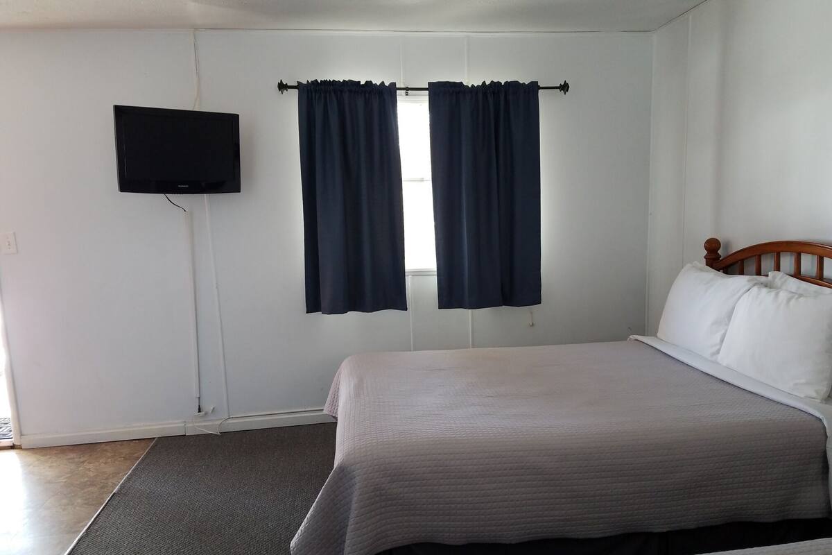 A bedroom with a bed, a television mounted on the wall, and a window with curtains.