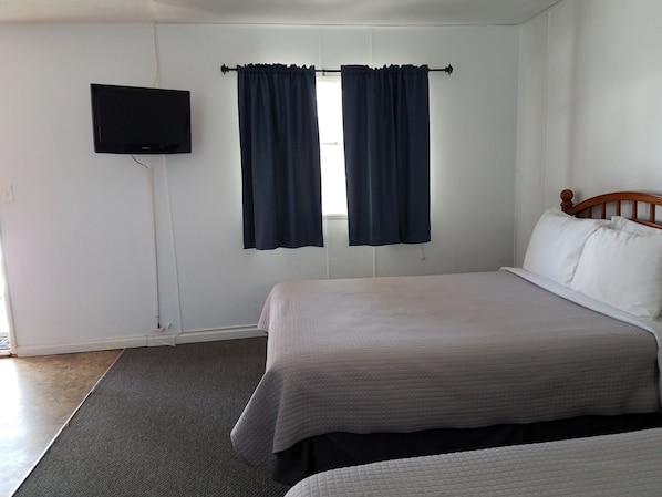 Un dormitorio con cama, televisor montado en la pared y ventana con cortinas.