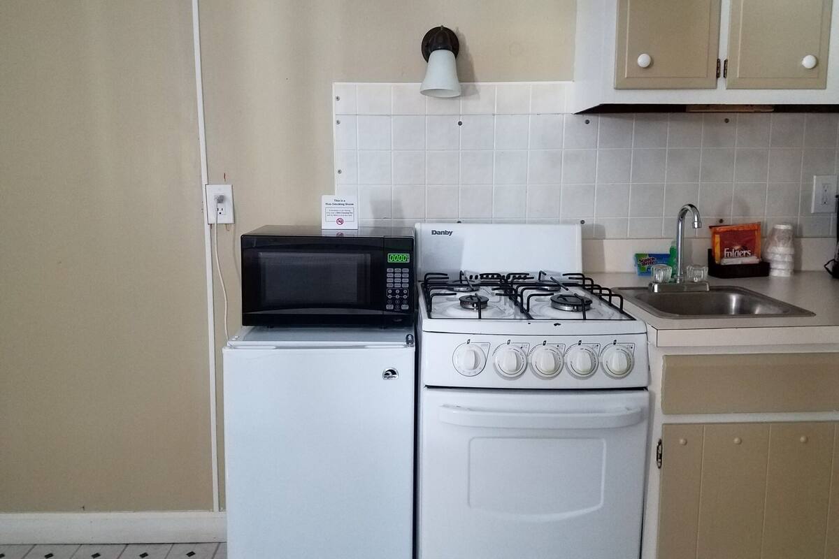 A compact kitchen with a white refrigerator, a black microwave, and a white gas stove.