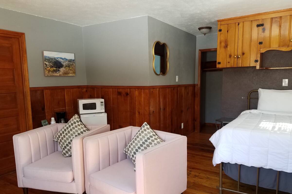 A room with a bed, two armchairs with patterned cushions, a microwave, and a coffee maker on a small table.
