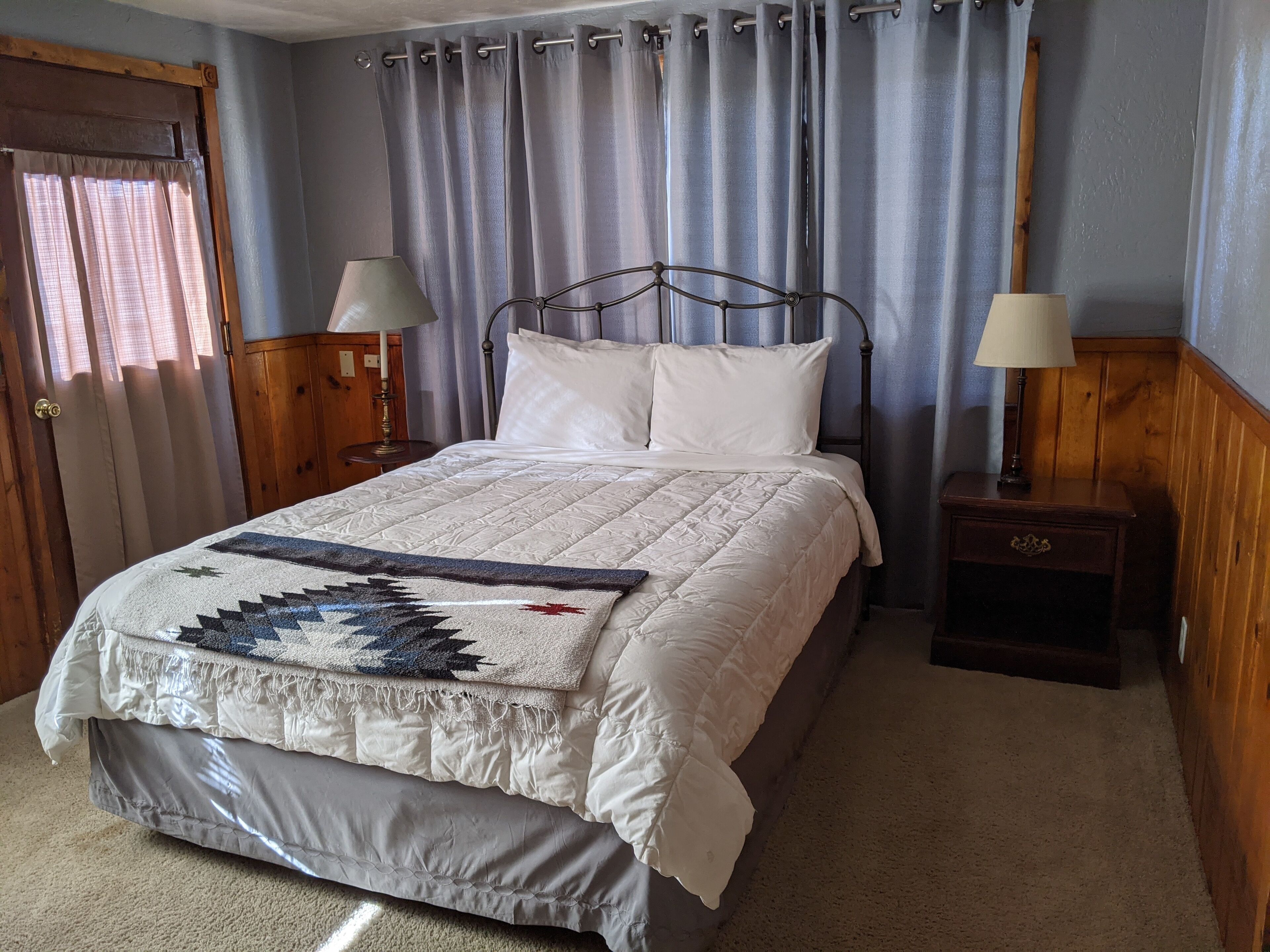 A neatly made bed with a quilt, two bedside lamps, and a wooden nightstand.