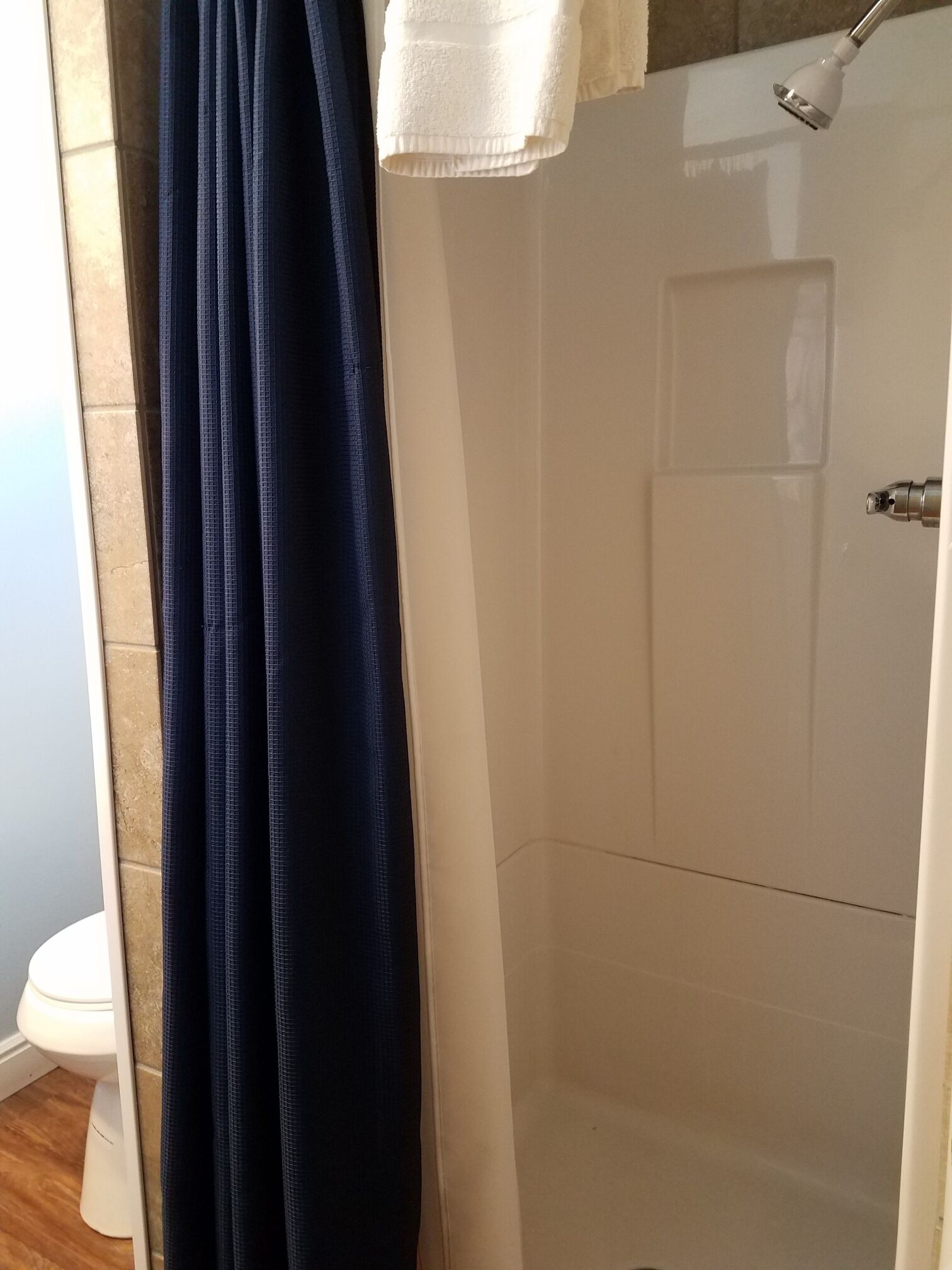 A bathroom with a white toilet, a dark blue shower curtain, and a white towel hanging on a rack.
