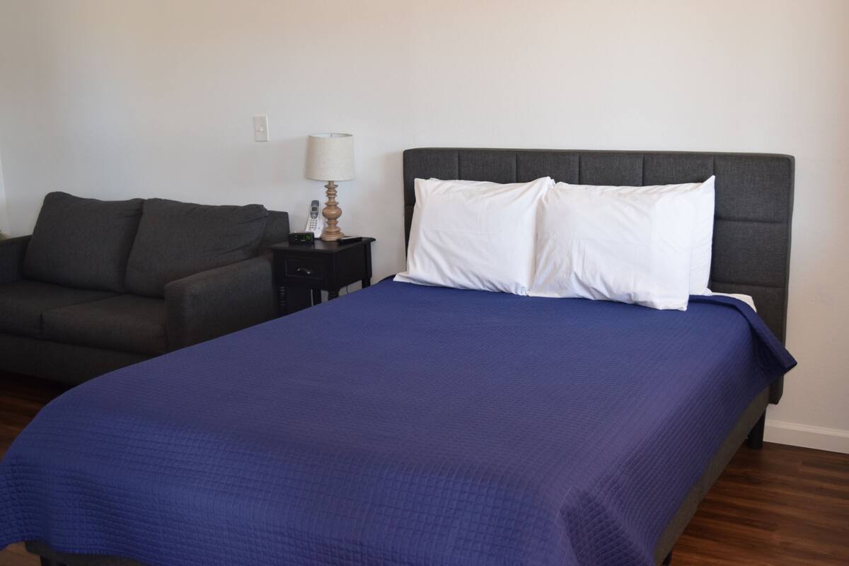 A hotel room with a bed, a nightstand, a lamp, and a sofa.