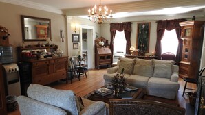 A traditional living room with a sofa, armchairs, and a coffee table. There is a chandelier, wooden furniture, and a large mirror on the wall. - Magnolia Manor B&B Inn (Williamsburg)