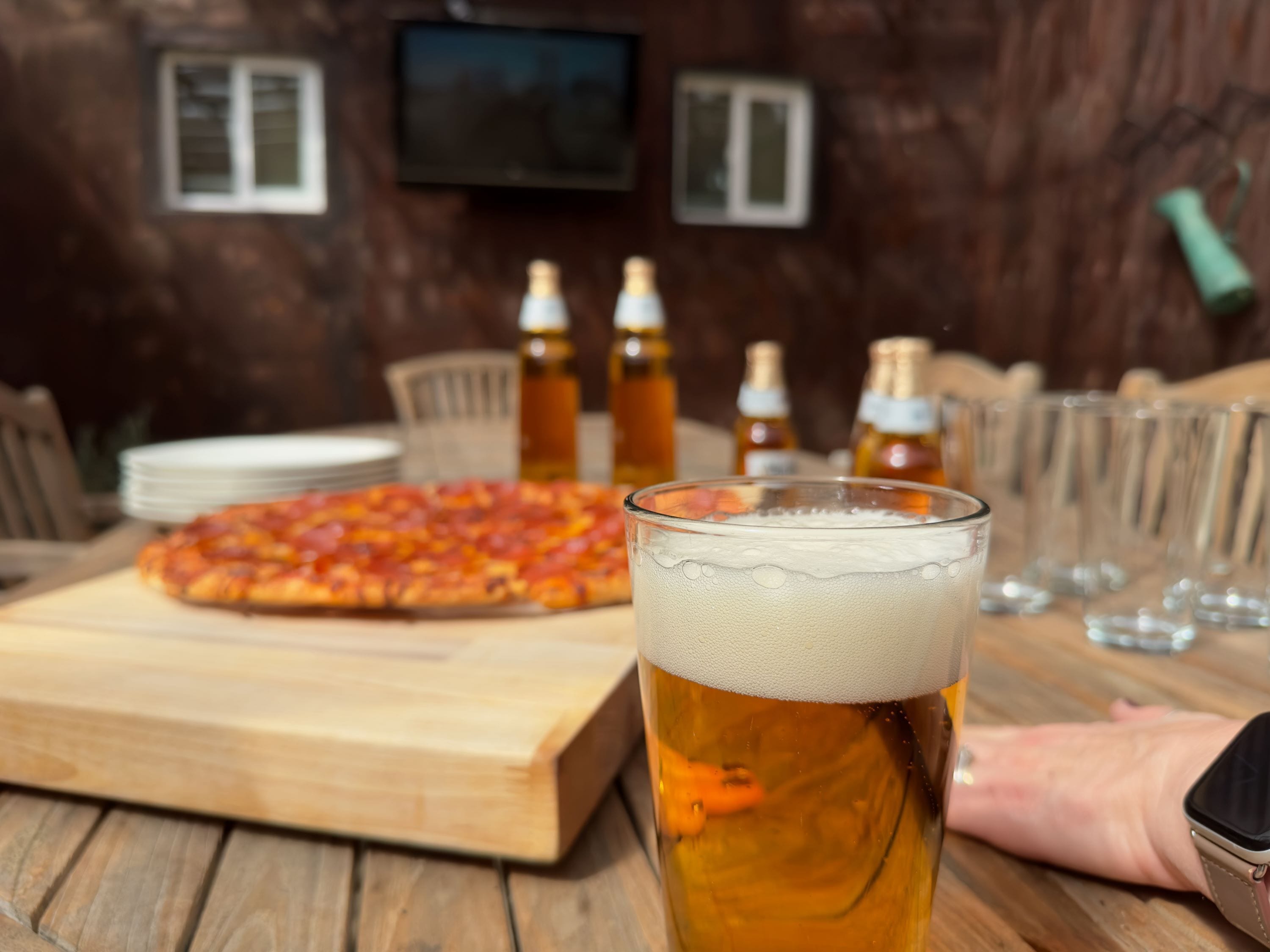 A wooden table with a pizza, a glass of beer, and empty glasses.