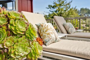 A sunlit outdoor seating area with a white metal table and two lounge chairs, one with a floral cushion.