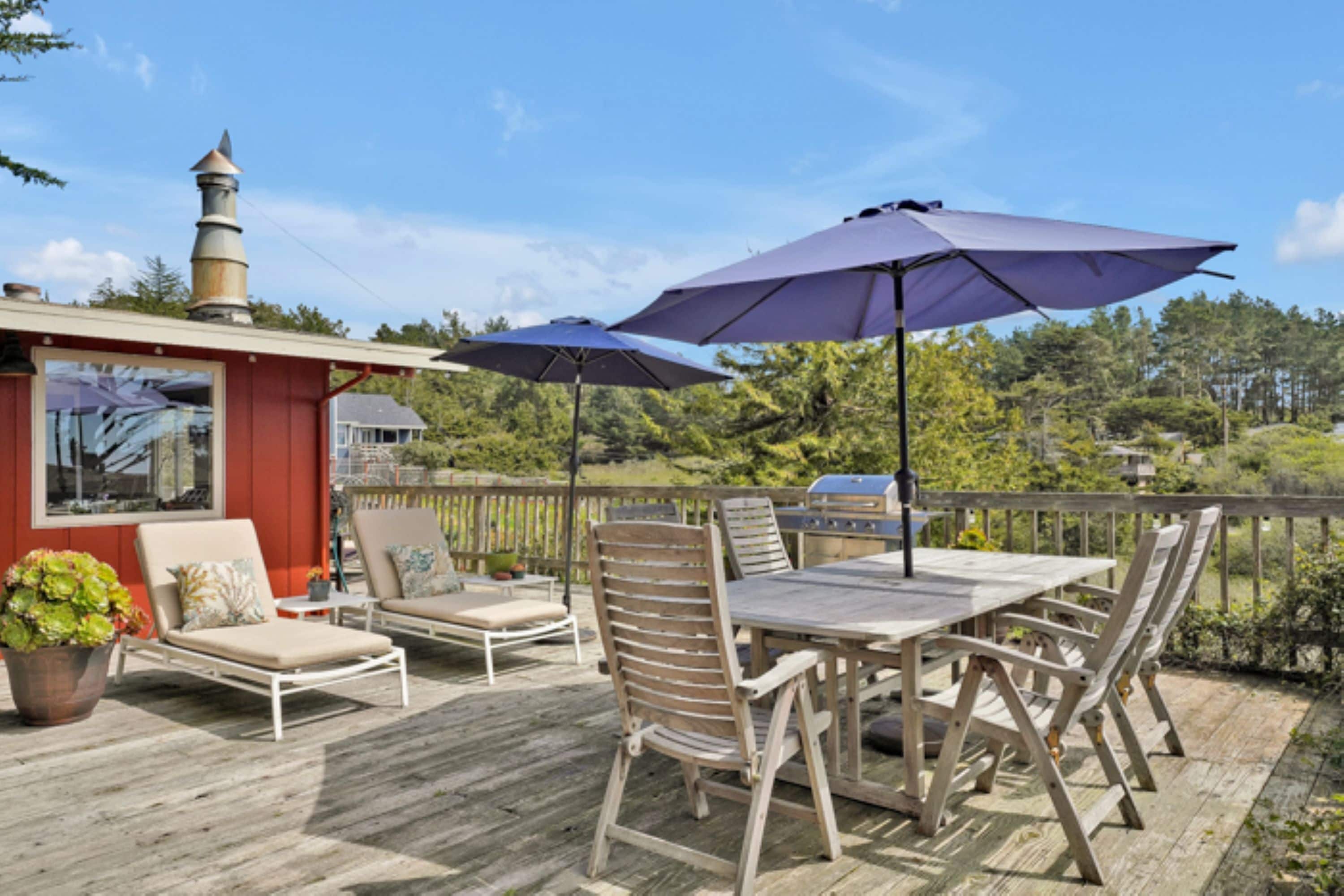 A wooden deck with outdoor furniture, including a table and chairs, and two umbrellas.