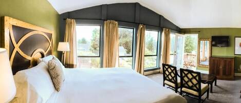 Une chambre d’hôtel avec un grand lit, un bureau, une chaise et une vue sur l’extérieur grâce à de grandes fenêtres.