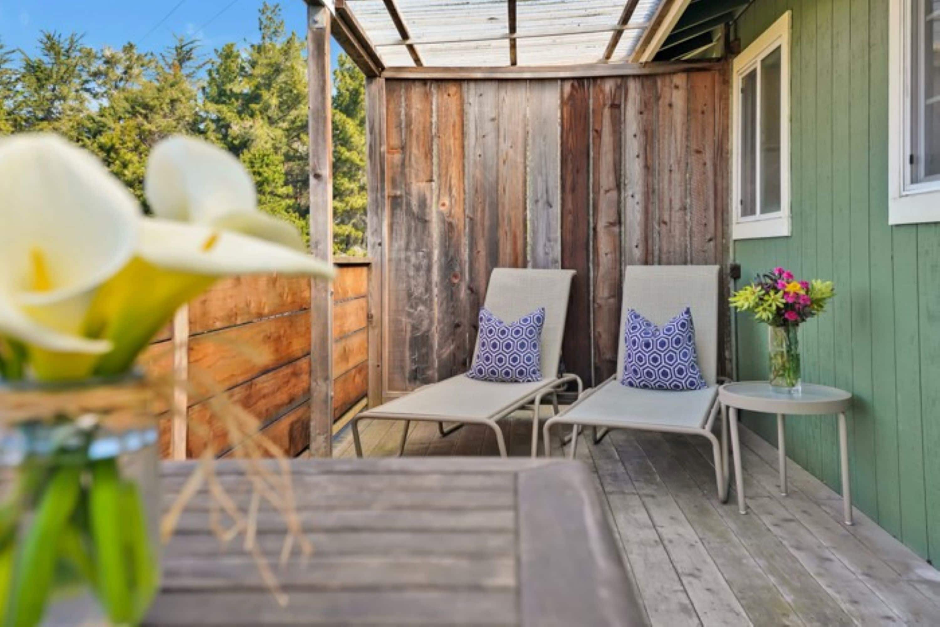 A wooden deck with two lounge chairs and a small table, surrounded by a wooden fence and a green wall.