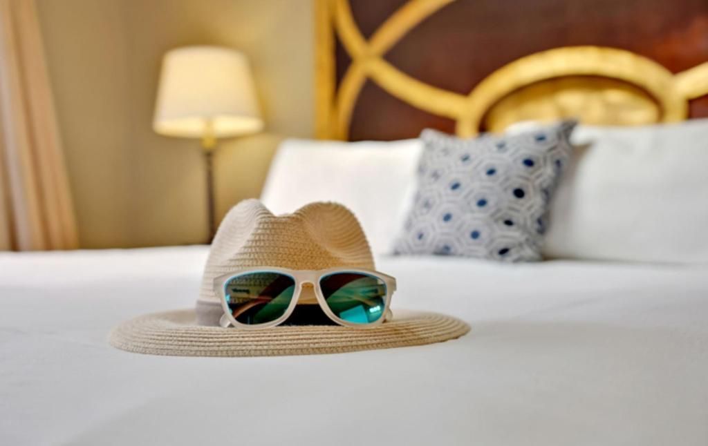 Una cama con una colcha blanca, un sombrero de paja y un par de gafas de sol.