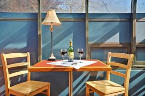 A table with a bottle and glasses, two wooden chairs, and a lamp.