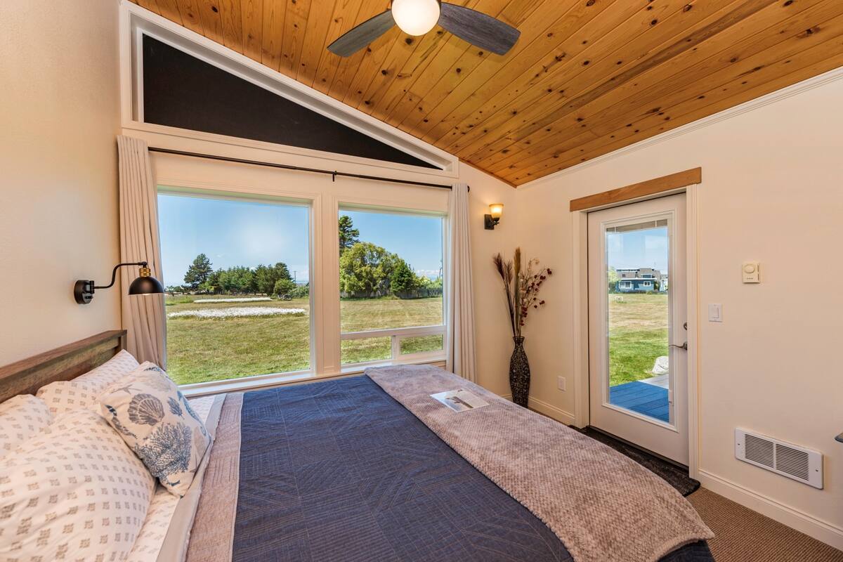 A bedroom with a large window, a ceiling fan, and a view of the outdoors.