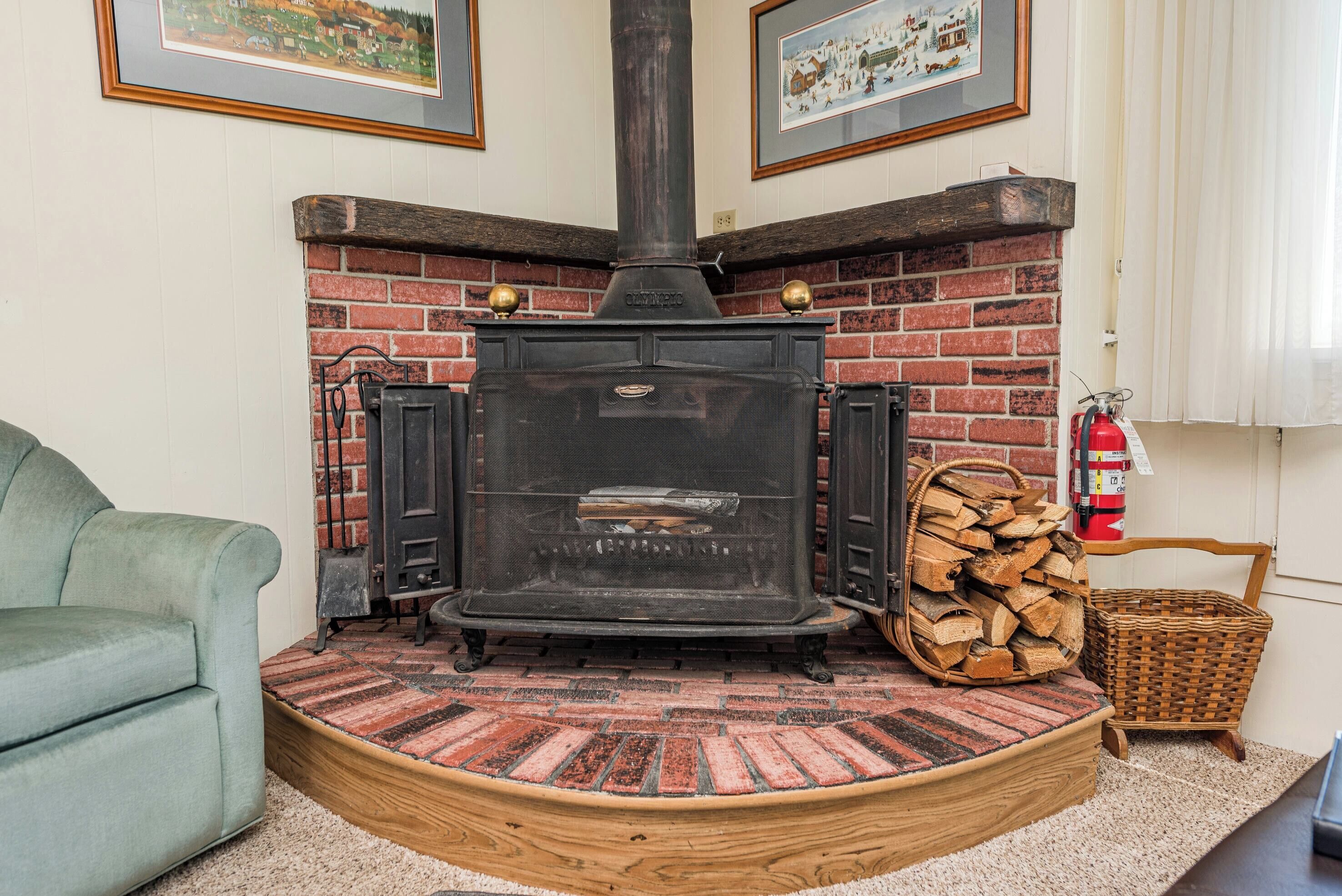 A cozy room with a brick fireplace, a green armchair, and a fire extinguisher.