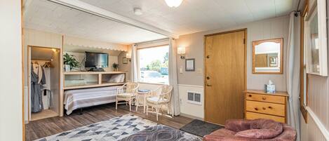 A room with a bed, a desk, a chair, a wardrobe, a television, and a window.