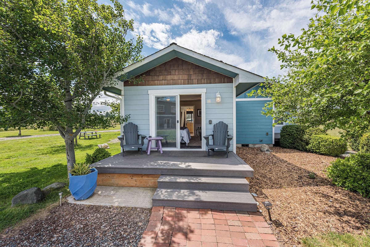 A small, single-story building with a porch, two Adirondack chairs, and a potted plant.
