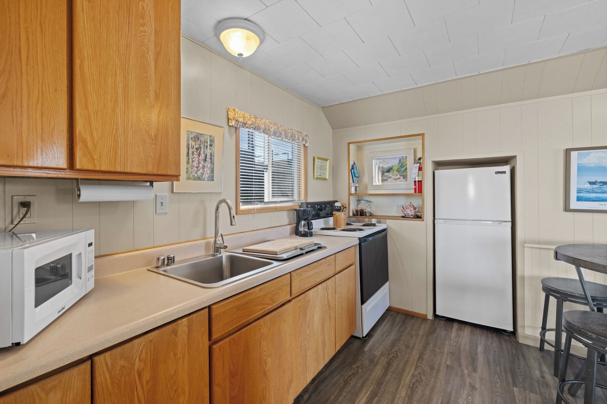 A compact kitchen with wooden cabinets, a built-in microwave, a sink, a stove, and a refrigerator.