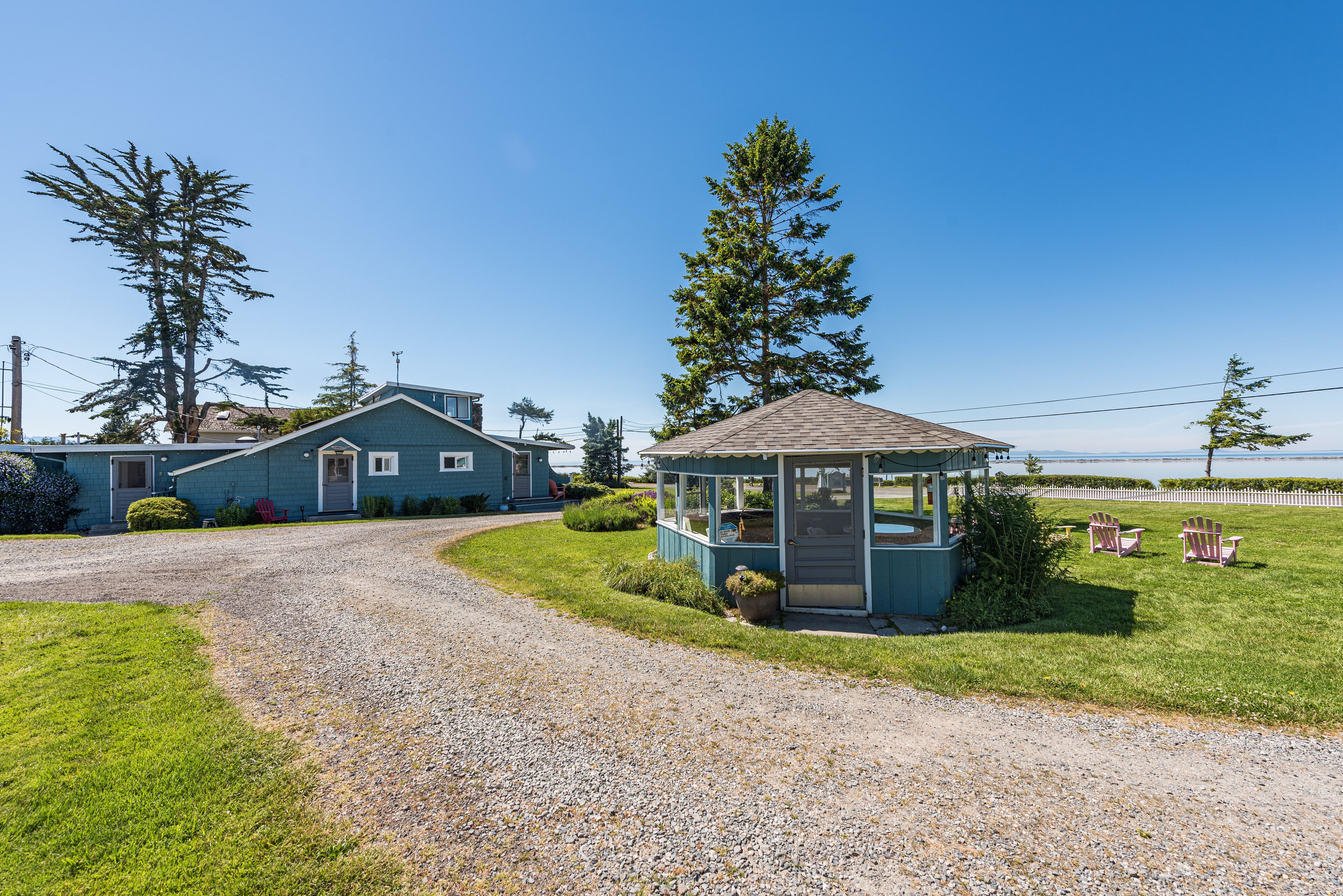 A house with a gravel driveway, a small gazebo, and two Adirondack chairs.