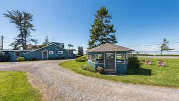 A house with a gravel driveway, a small gazebo, and two Adirondack chairs.