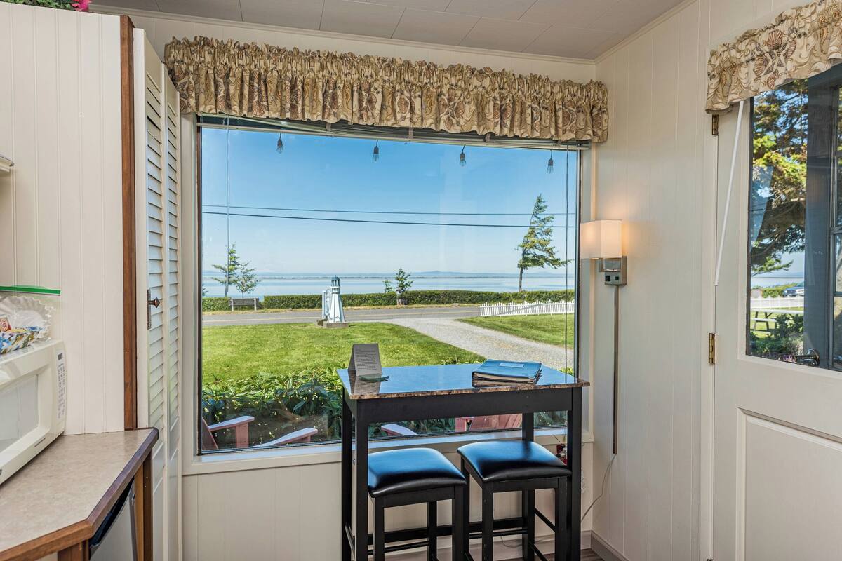 A room with a large window overlooking a scenic view, a small table with chairs, and a lamp.