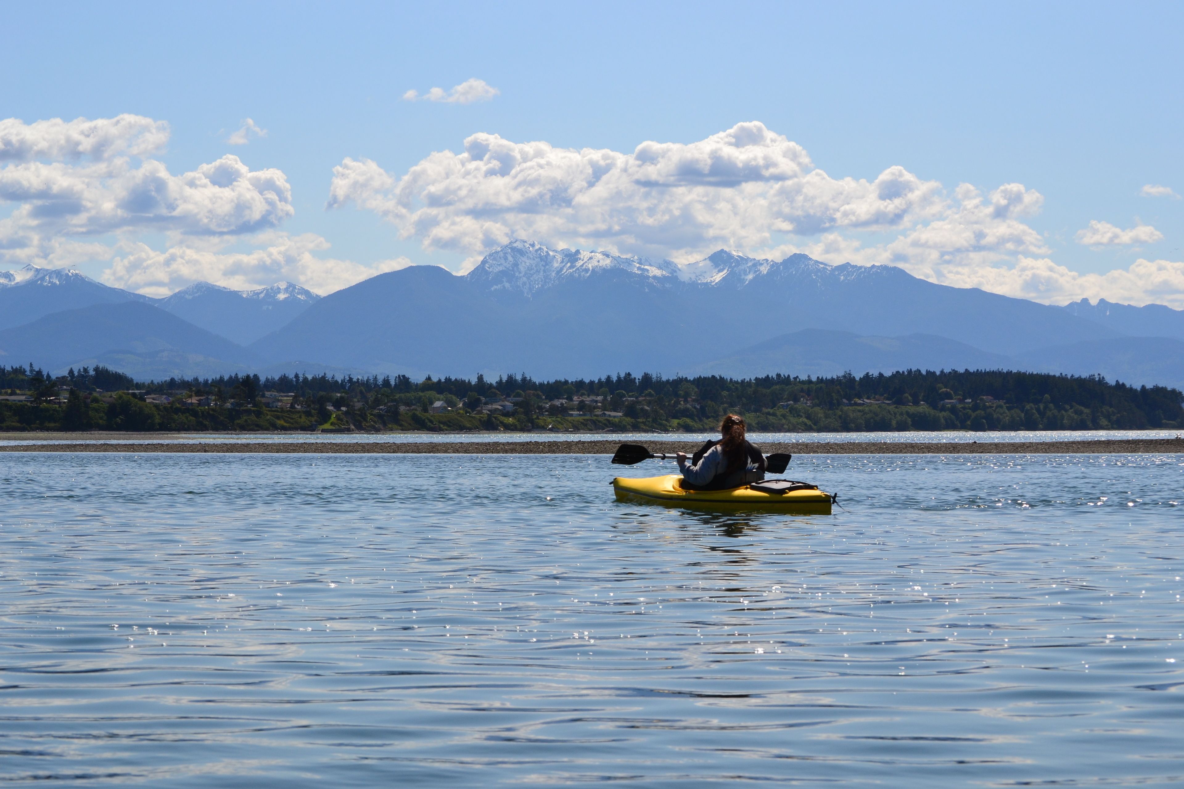 A kayaker on a calm lake with mountains in the background.