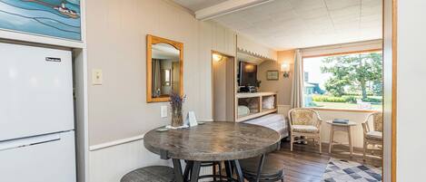 A compact kitchen with a dining area, a refrigerator, a round table with stools, and a view of the outdoors through a window.