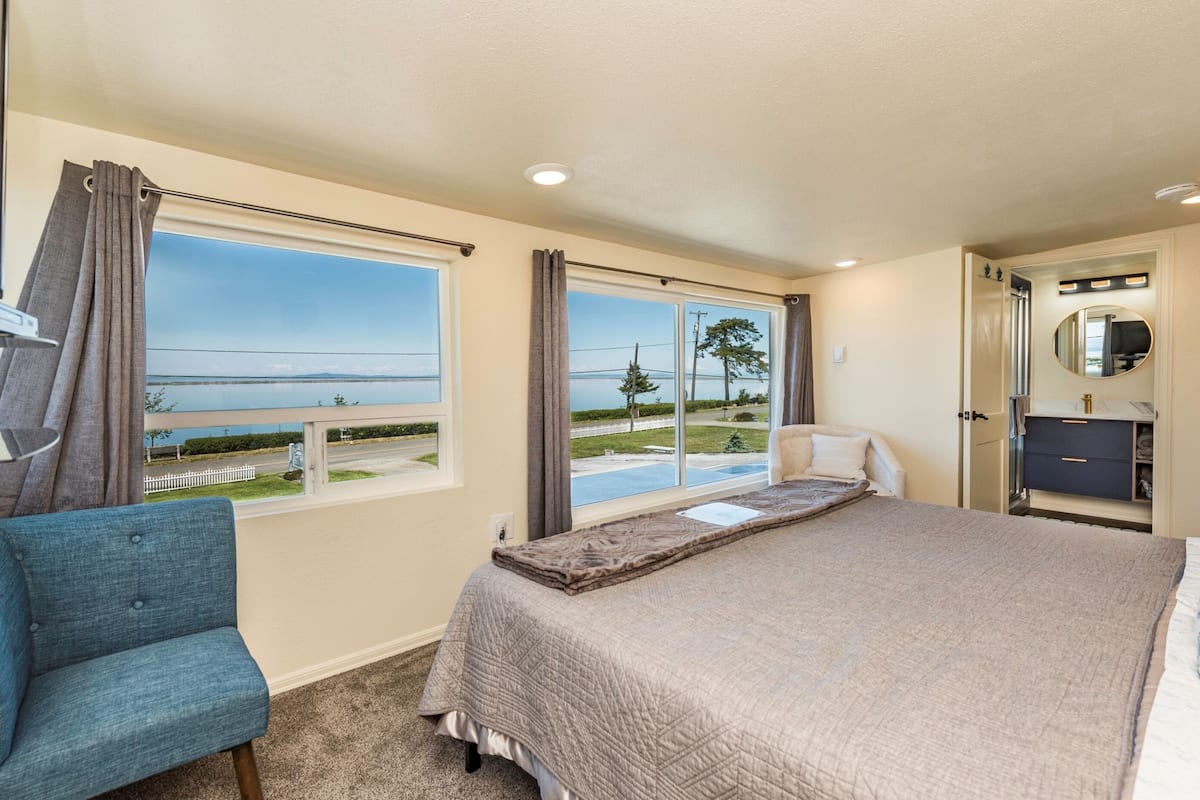 A bedroom with a bed, a chair, a dresser, and a view of the beach.