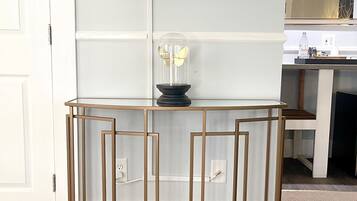 Una sala de estar moderna con un televisor de pantalla plana montado en la pared, una mesa de centro con cubierta de vidrio y un objeto decorativo, y un mueble consola de madera con diseño geométrico.