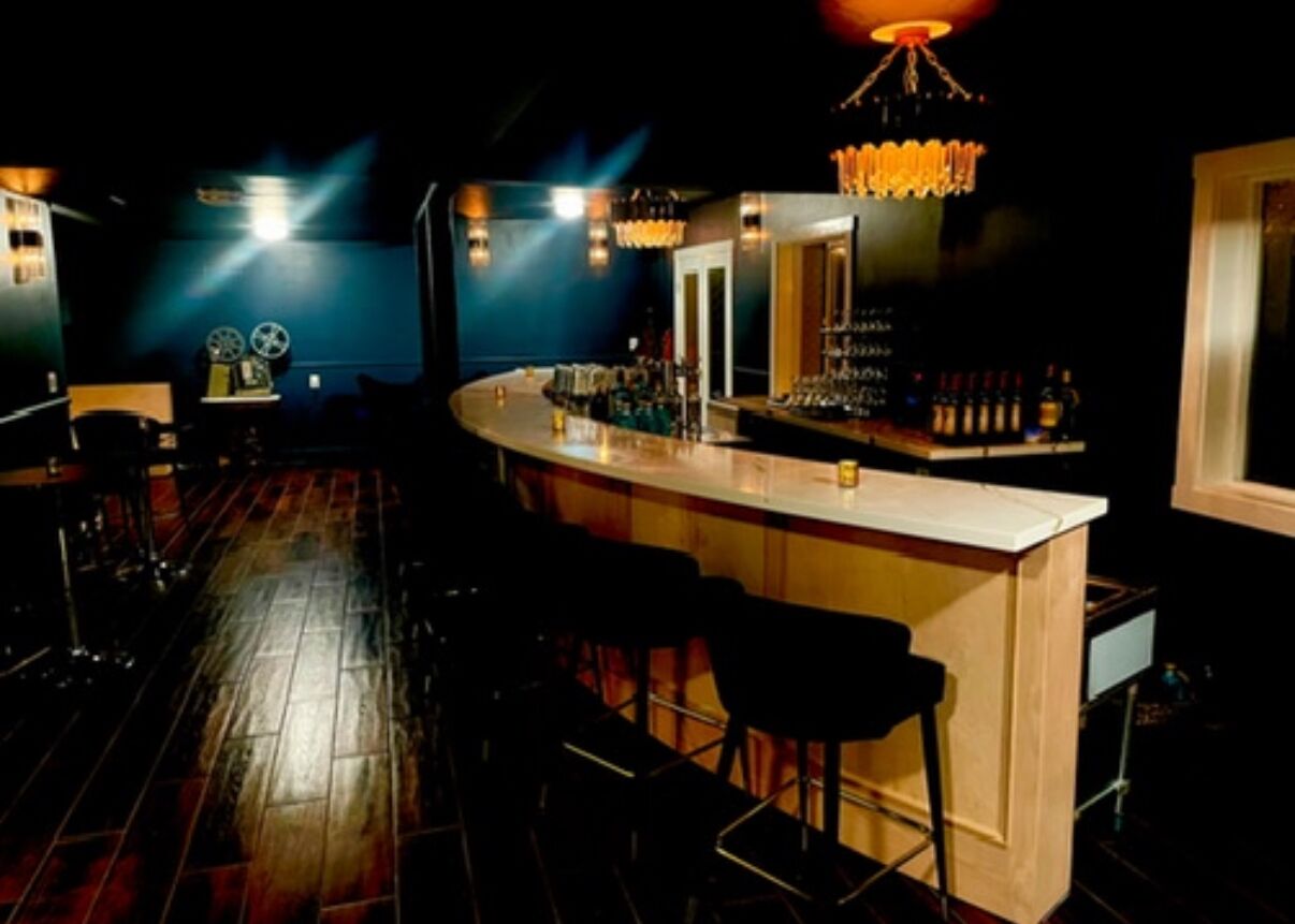 Una zona de bar con mostrador de madera, taburetes negros y una lámpara de araña.