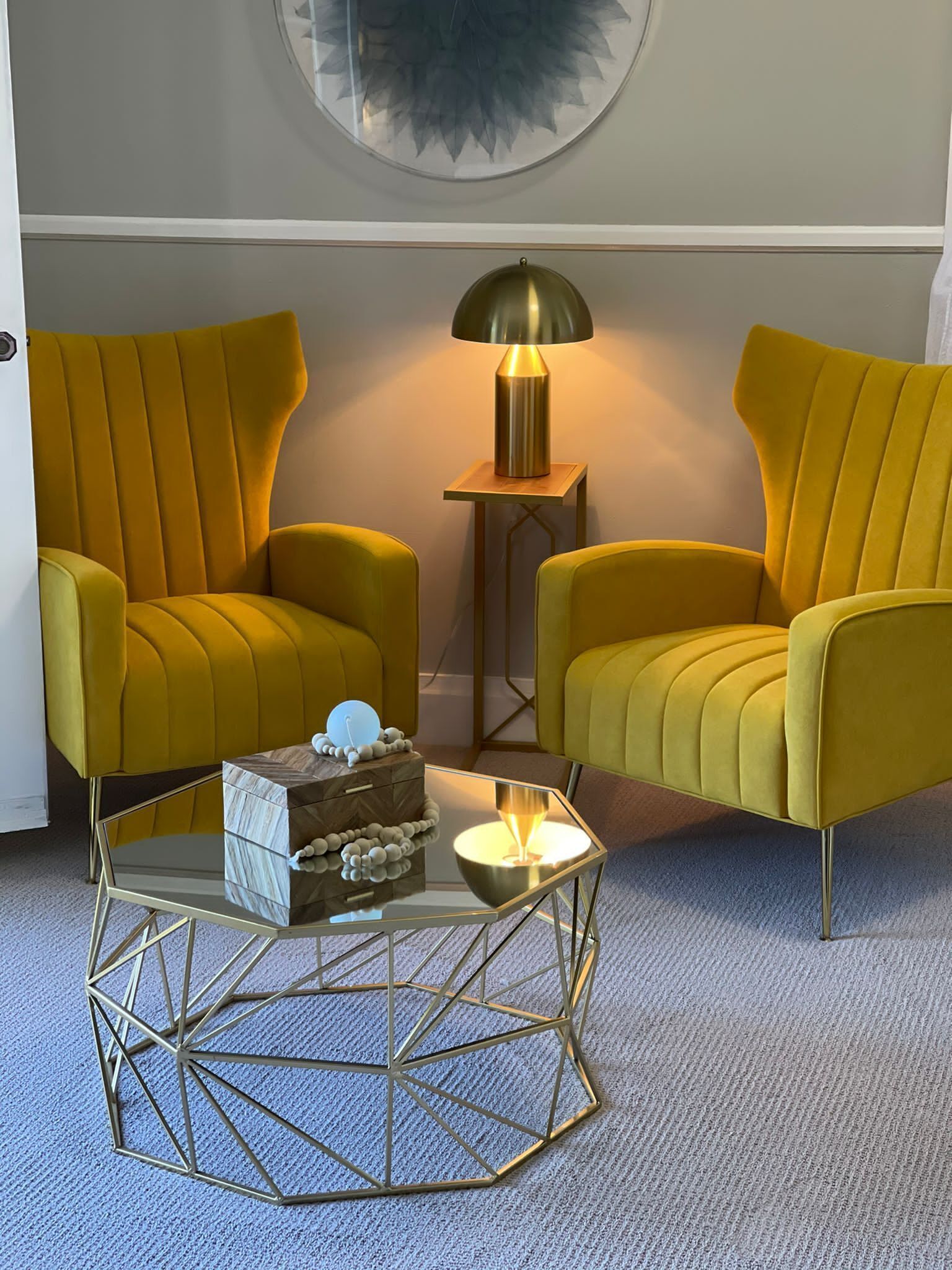 A room with two mustard yellow armchairs, a small side table with a lamp, and a geometric coffee table.