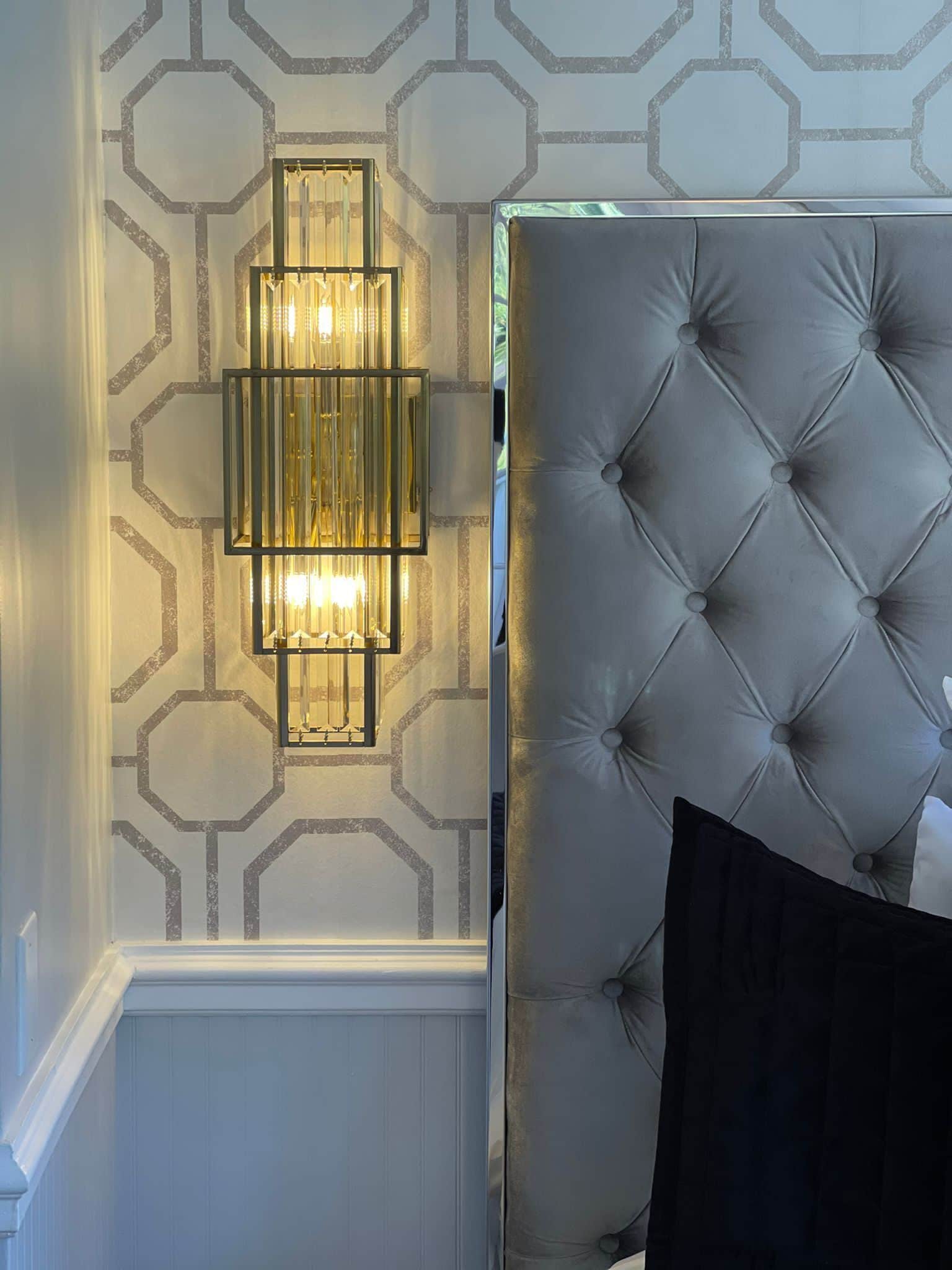 A tufted headboard with a black pillow, a wall-mounted light fixture, and a geometric patterned wall.