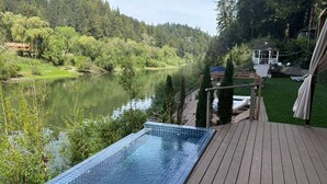 A swimming pool on a wooden deck with a view of a lake and forest.