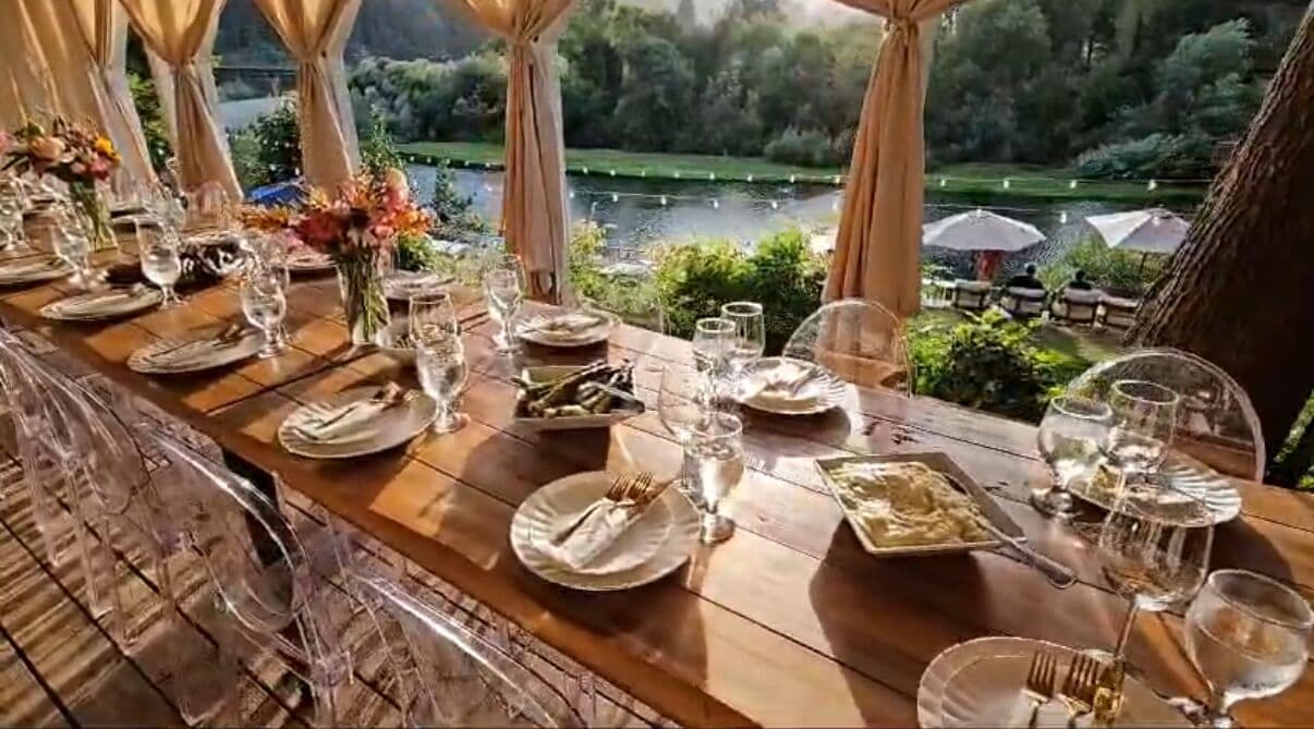 Mesa de comedor lista para una comida, con vistas a un lago y follaje.