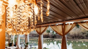 An outdoor dining area with a view of a lake, covered by a wooden roof, and decorated with hanging crystal lights.